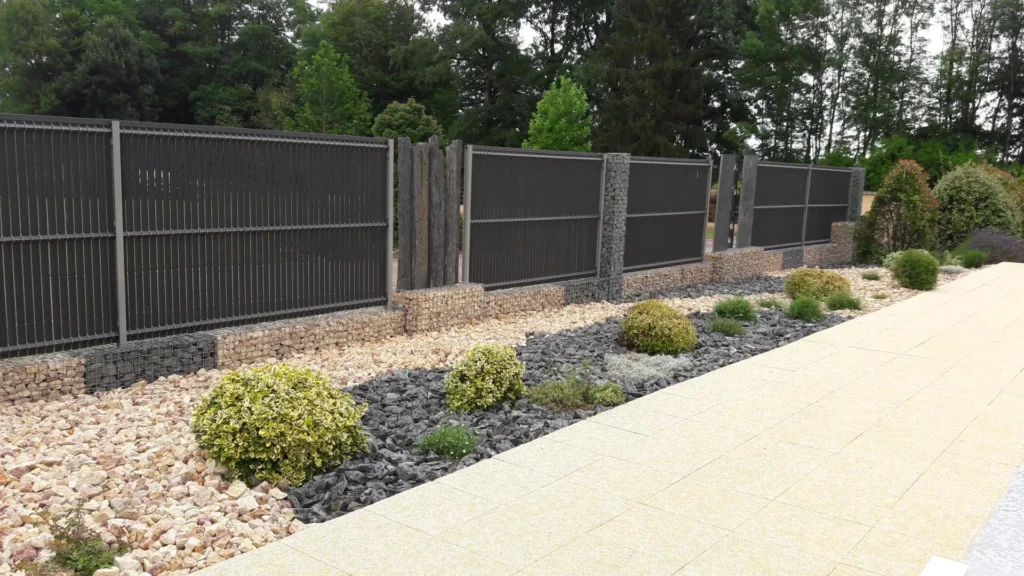 Clôture contemporaine sombre intégrée à un aménagement paysager avec gabions et végétaux