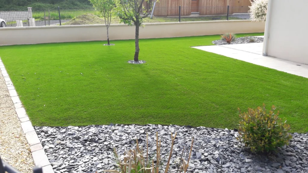 Gazon aménagé dans un jardin paysager avec arbres, massifs minéraux et terrasse