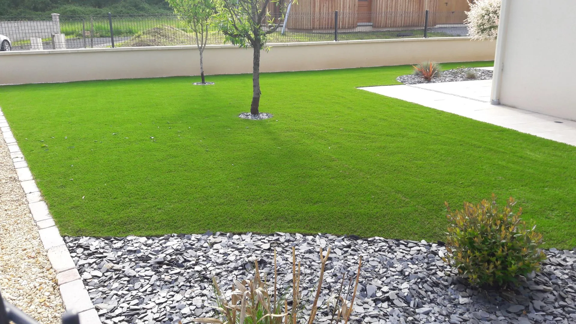 Gazon aménagé dans un jardin paysager avec arbres, massifs minéraux et terrasse
